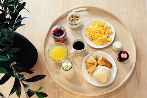 Bandeja de desayuno con huevos revueltos, croissants, un vaso de zumo de naranja, una taza de café y un tarro de mermelada.
