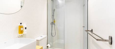 Un baño moderno con cabina de ducha de vidrio, un lavabo blanco y un inodoro.