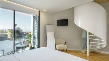 Ein modernes Schlafzimmer mit einem großen Bett, einem weißen Stuhl, einem an der Wand befestigten Fernseher und einer Wendeltreppe.