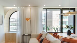 A modern living room with a sofa, a dining table, and a large window with curtains. - Feel Porto Corporate Housing Boavista (Porto)