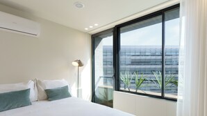A modern bedroom with a large bed, a window with a view of a building, and a floor lamp. - Feel Porto Corporate Housing Boavista (Porto)