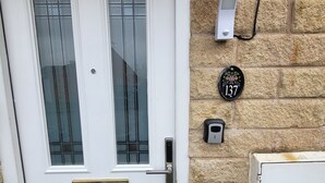 Eine weiße Haustür mit Messingbeschlägen, einem Glasfeld und einem kleinen Briefkasten an der Wand.