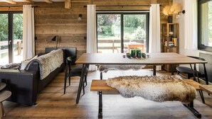 Un salon moderne avec un plafond en bois, de grandes fenêtres, un canapé, une table à manger et un plaid en fourrure.