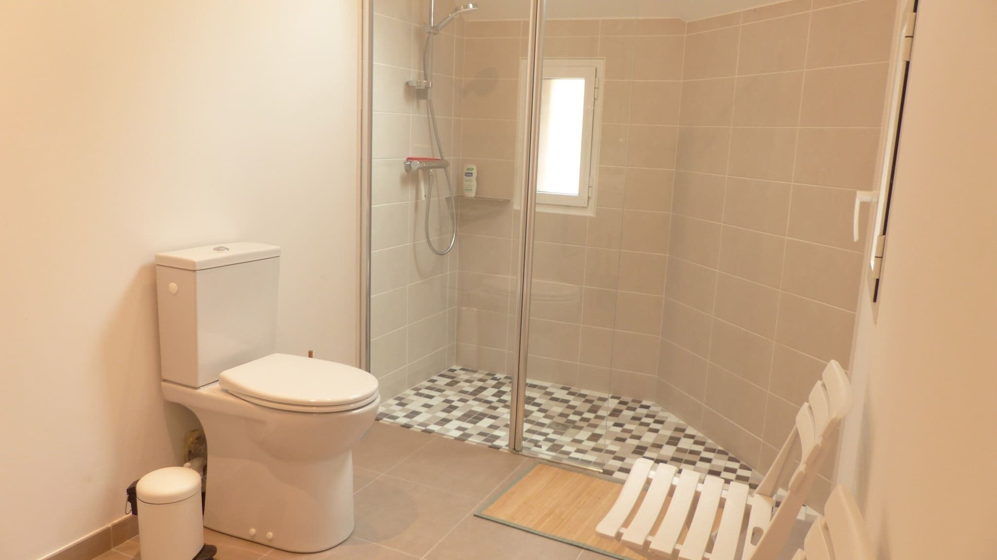 Un baño con inodoro, ducha con puerta de cristal y suelo a cuadros.