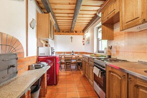 A kitchen with wooden cabinets, a red refrigerator, a tiled floor, and a cross on the wall. - Podhamer Wellness Vineyard Cottages (Ljutomer)