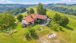 A house with a red roof, surrounded by lush greenery and vineyards. - Podhamer Wellness Vineyard Cottages (Ljutomer)