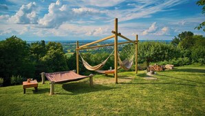 A hammock set up on a wooden structure with a view of a grassy landscape and trees. - Podhamer Wellness Vineyard Cottages (Ljutomer)