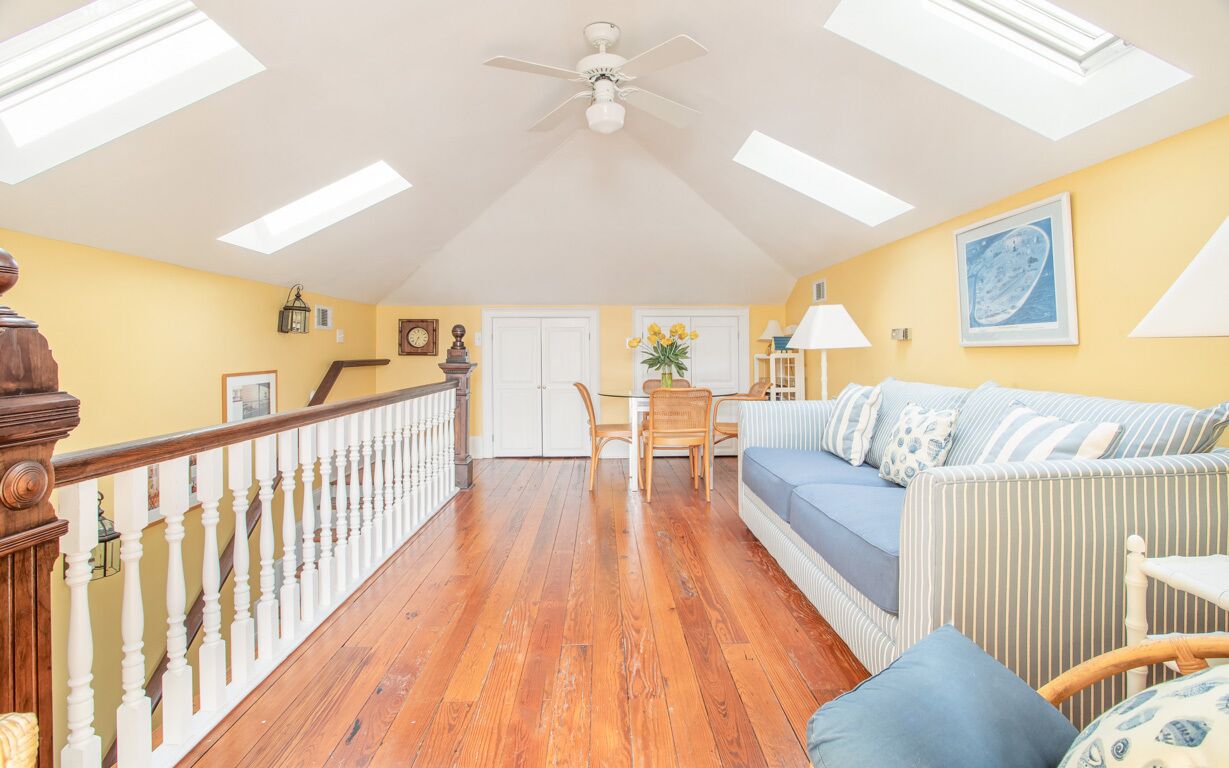 Une pièce spacieuse avec un plancher en bois, un canapé bleu, une table à manger avec des chaises et un escalier doté d’une rampe blanche.