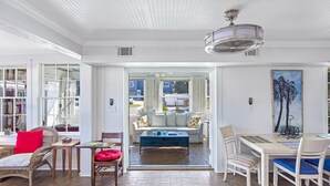 Ein geräumiges Wohnzimmer mit weißer Decke, einem blauen Couchtisch und einem Essbereich mit weißen Stühlen und einem Tisch.