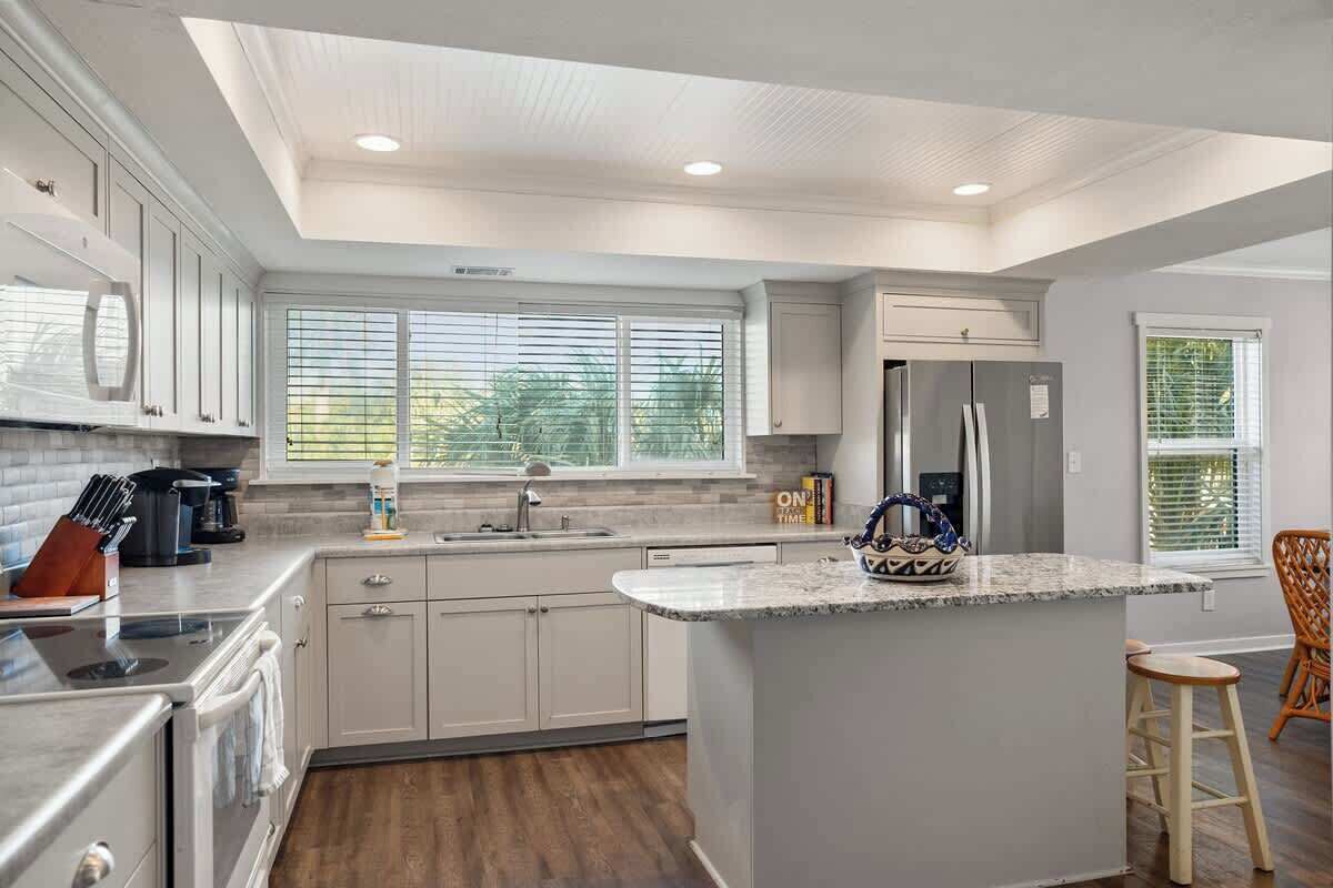 A modern kitchen with white cabinets, a central island, and a built-in oven.