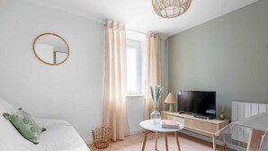 A modern, well-lit bedroom with a bed, a TV, and a small table with a lamp.