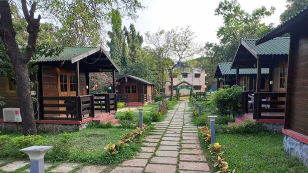A pathway leading to wooden cabins with a stone-tiled walkway and potted plants. - Cocorico Stay Ya (Alibag)