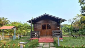 A wooden cabin with a red roof, a front porch, and a small garden area with stepping stones leading to the entrance. - Cocorico Stay Ya (Alibag)