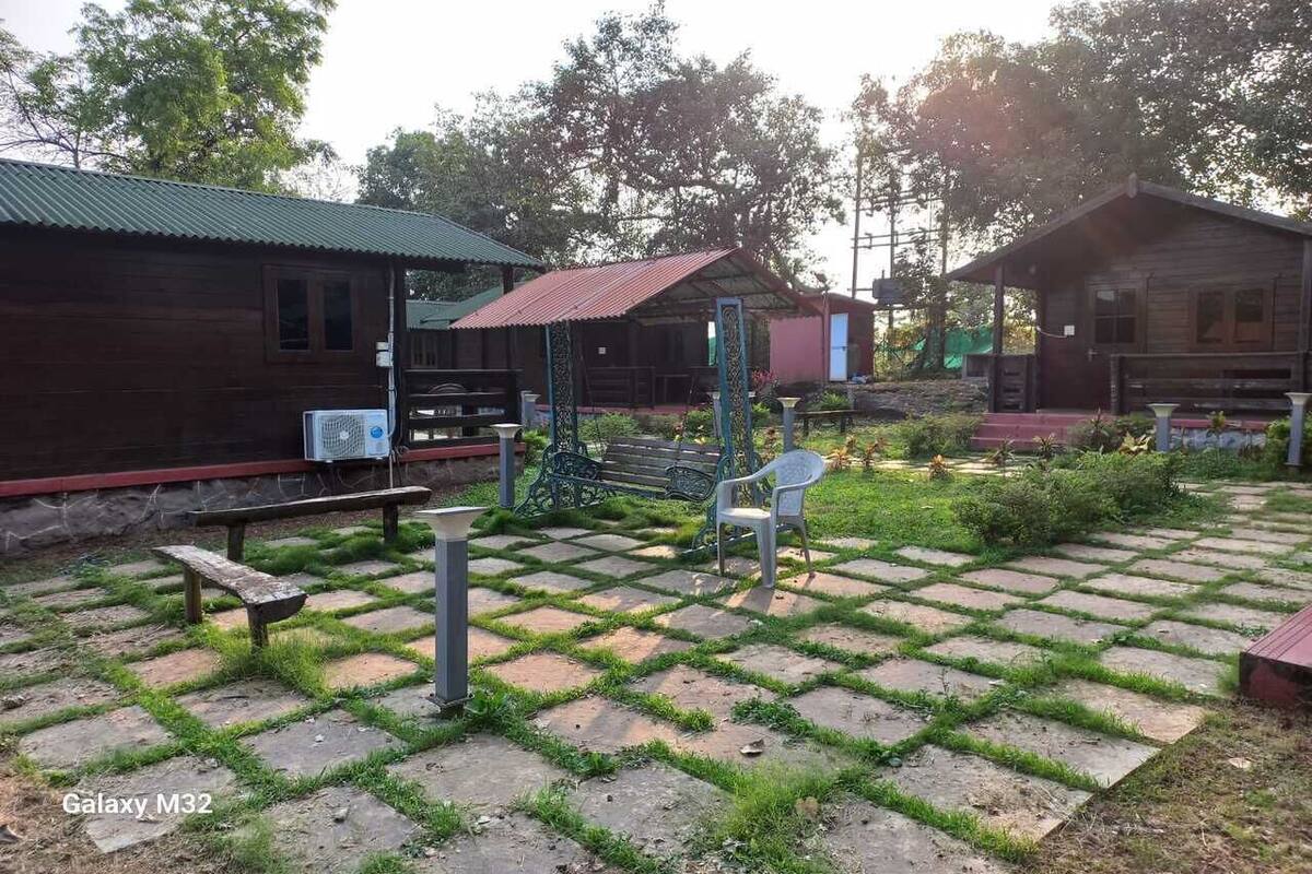 A rustic outdoor area with wooden cabins, a paved patio with benches, and a small garden.