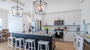 A modern kitchen with white cabinets, a central island with bar stools, stainless steel appliances, and pendant lighting. - Luxury Waterfront 4BR Home w/ Pool & Hot Tub (Cape Coral)