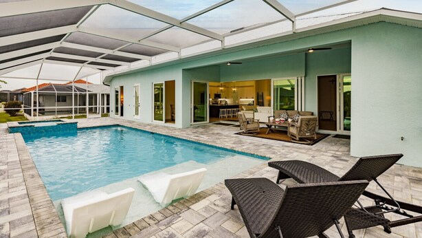 An indoor swimming pool with a covered patio area, a dining table, and lounge chairs. - Luxury Waterfront 4BR Home w/ Pool & Hot Tub (Cape Coral)