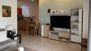 A modern living room with a sofa, TV, and a dining area with a table and chairs. - Angelos elegant summer house  (Kassandra)