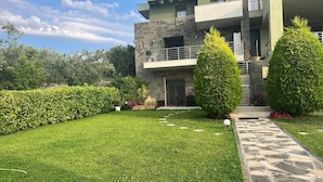 A modern two-story building with a stone facade, a balcony, and a well-maintained lawn with hedges. - Angelos elegant summer house  (Kassandra)
