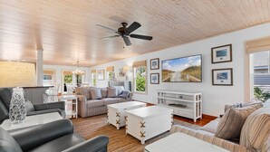 Un vaste salon doté d’un ventilateur de plafond, d’un grand téléviseur à écran plat et d’un meuble de rangement blanc pour les appareils multimédias. On y trouve plusieurs coins salon, notamment un canapé et un fauteuil.