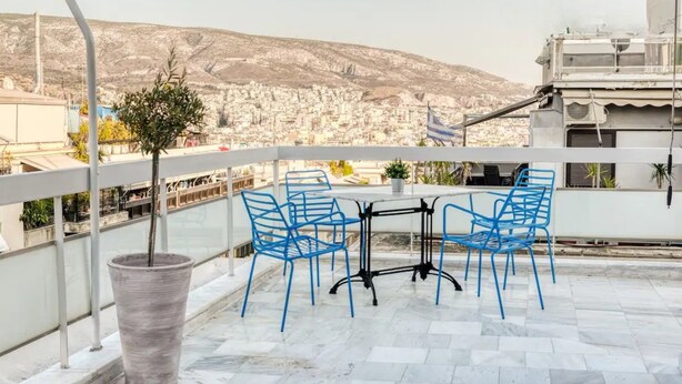 Een terras met een tafel en blauwe stoelen, met uitzicht op een stadsgezicht en een heuvel op de achtergrond.