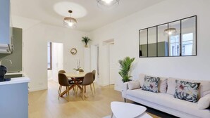 Un salon moderne avec un canapé blanc, une table à manger avec des chaises et une table basse. Un grand miroir est accroché au mur et une plante est posée sur le sol.