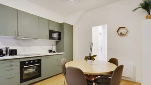 Une cuisine moderne avec des meubles de couleur vert clair, un four encastré et un four à micro-ondes. On y trouve une table à manger avec quatre chaises et une plante en pot.