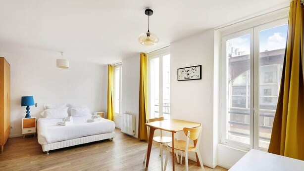 Een hotelkamer met een bed, een tafel met stoelen, een raam met gordijnen en een radiator.