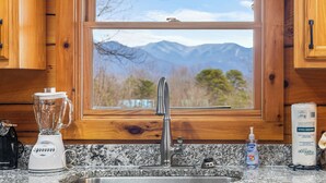 A kitchen with wooden cabinets, a granite countertop, a blender, a faucet, and a window with a mountain view. - Gorgeous Views, Game Room, Sauna, True Log Cabin! | Free Attractions! (Gatlinburg)