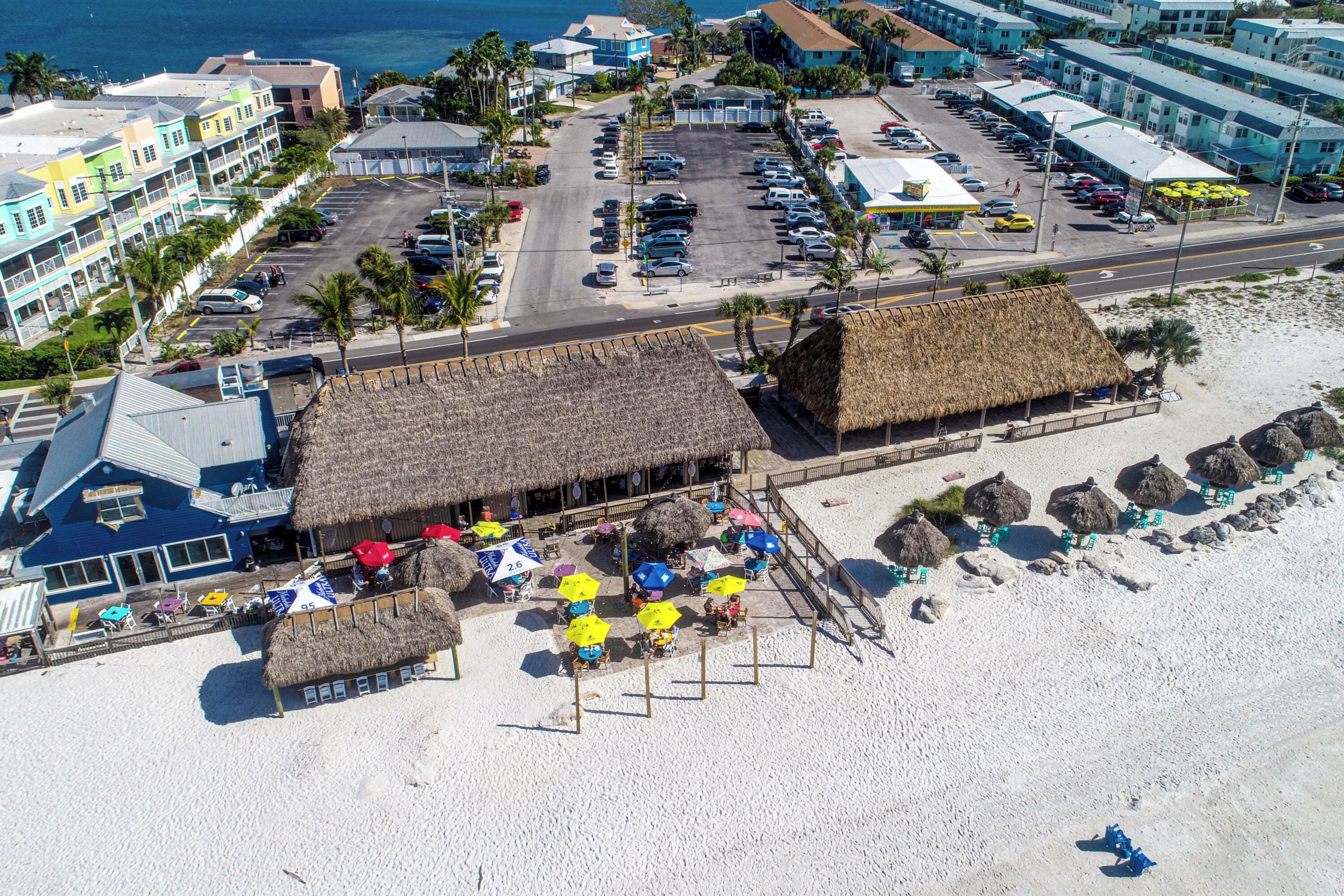 A beachside hotel with a parking lot, beach umbrellas, and thatched-roof structures.