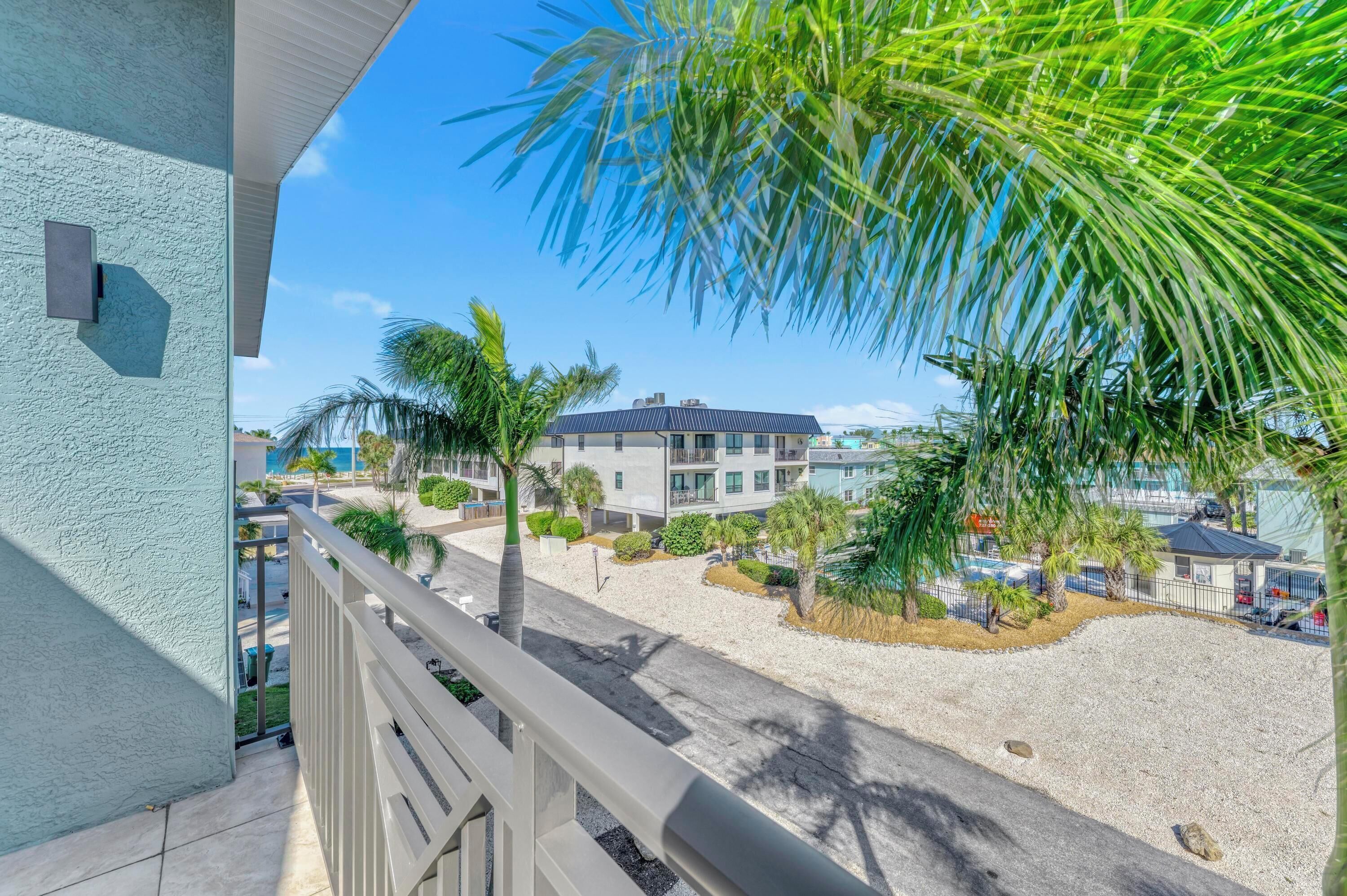 A balcony with a view of a residential area, including a building with a flat roof and a parking lot with palm trees.