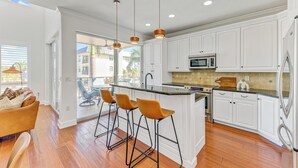 Una cocina moderna con armarios blancos, una isla central con taburetes de bar, un microondas y un refrigerador.