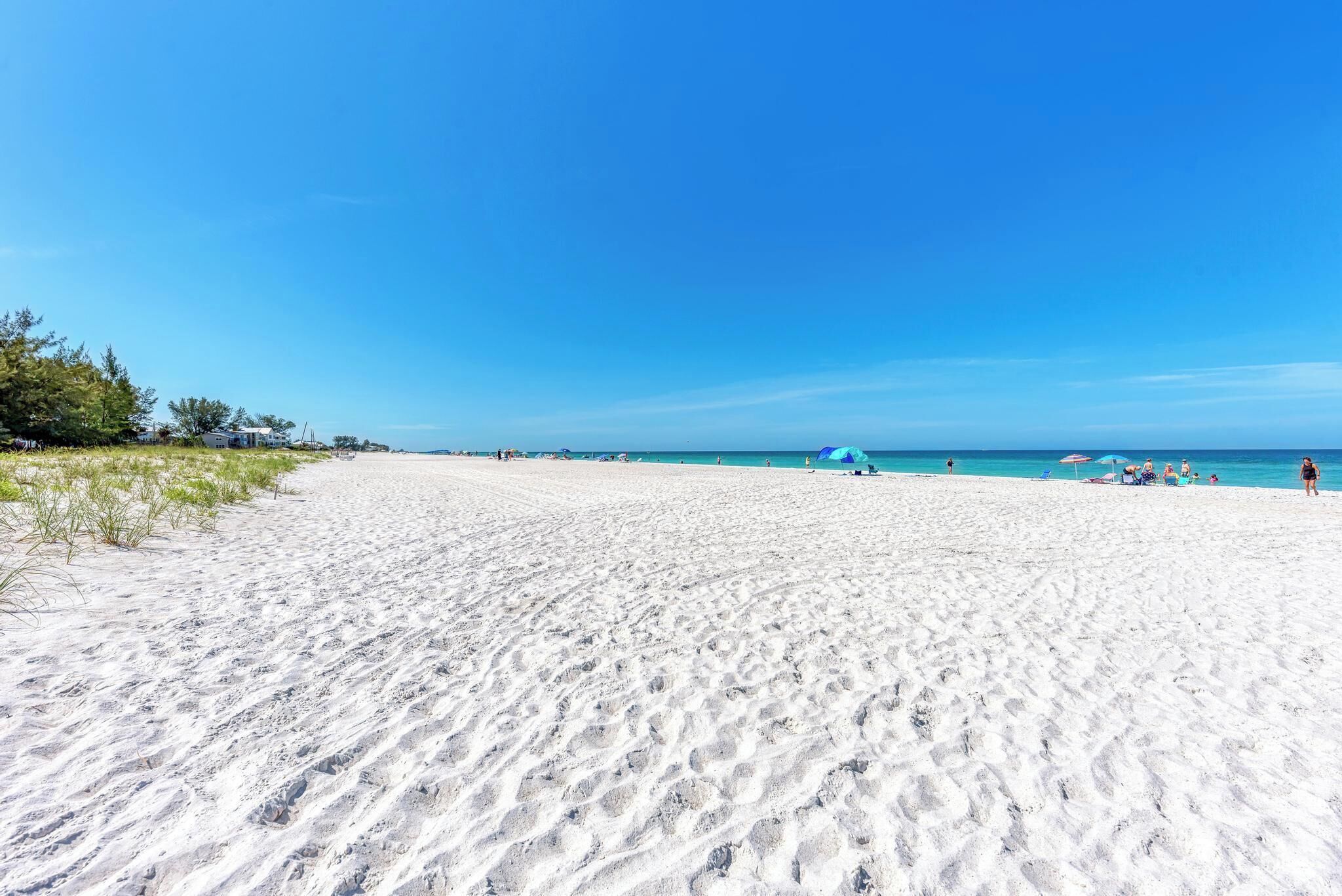 A wide sandy beach with clear blue skies and distant buildings.
