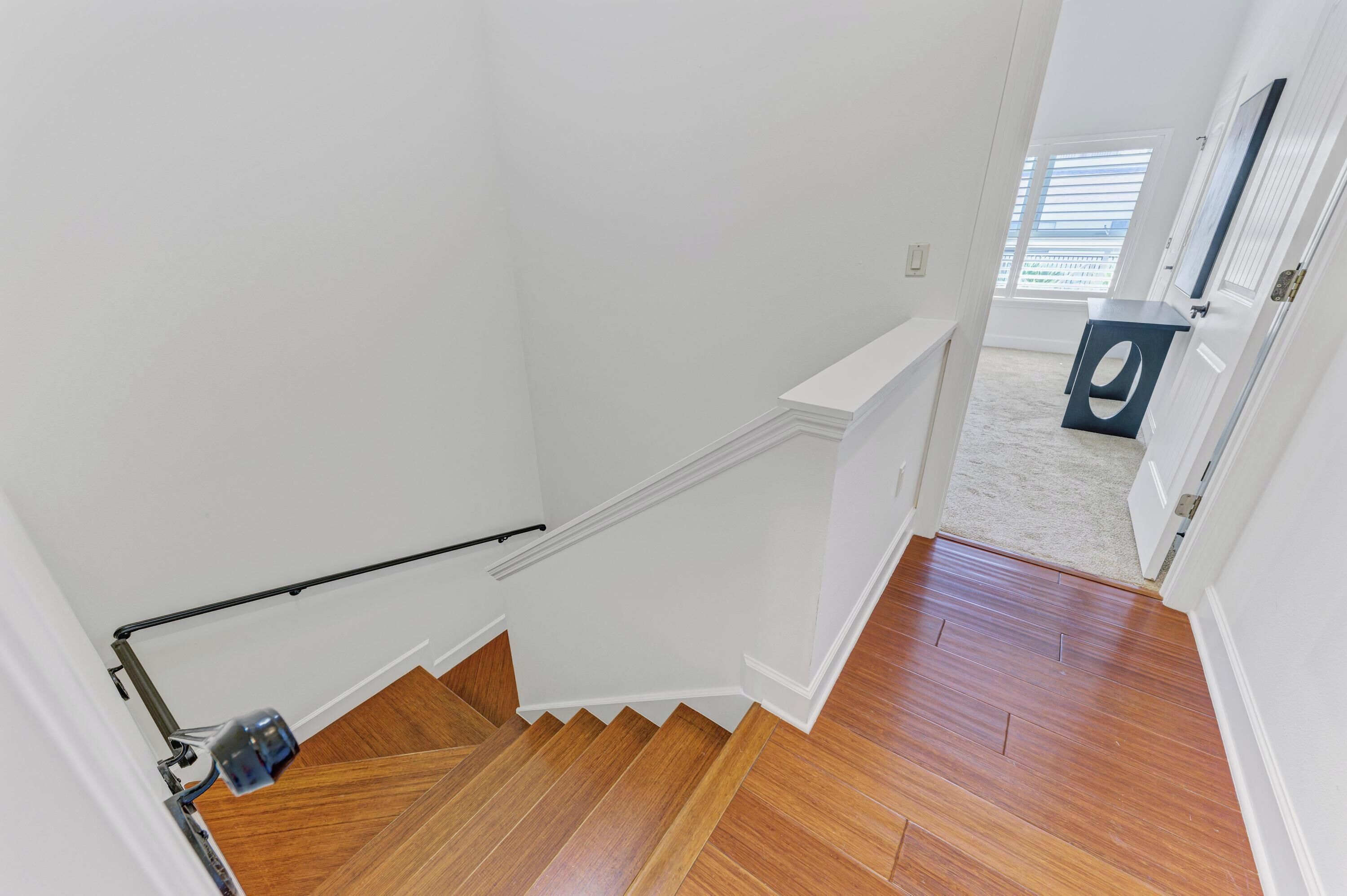 A staircase with wooden steps and a handrail, leading to a room with a white door and a window with blinds.