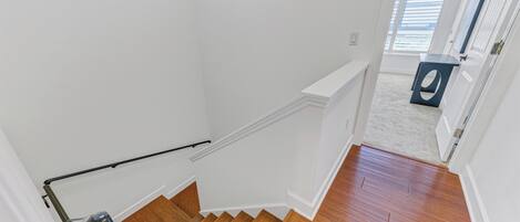 A staircase with wooden steps and a handrail, leading to a room with a white door and a window with blinds.