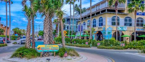 A street corner with a sign for Historic Bridge Street, palm trees, and a building with multiple stories and balconies.