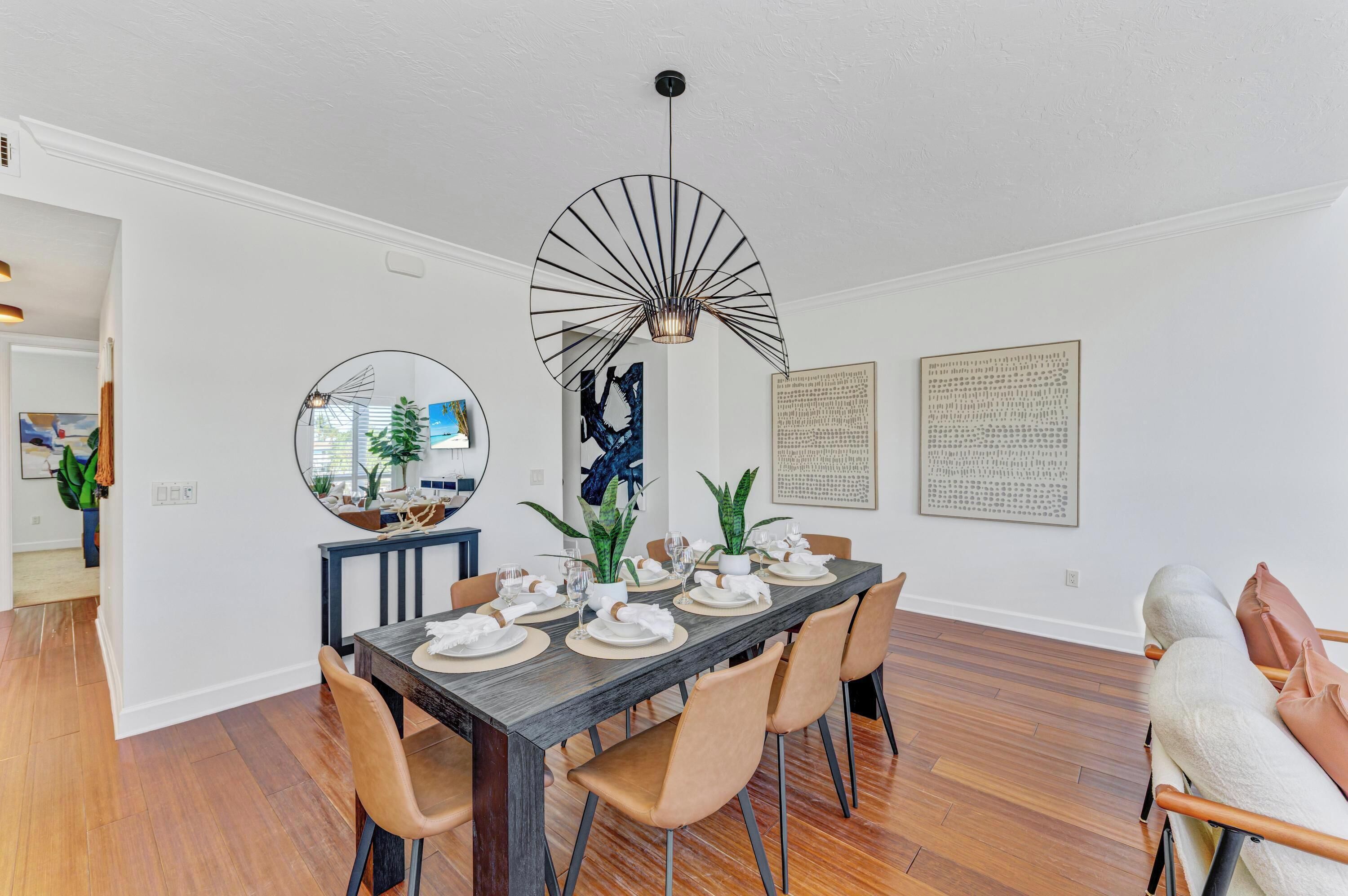Une salle à manger avec une longue table dressée pour six personnes, entourée de chaises, et un ventilateur-plafonnier moderne au-dessus.