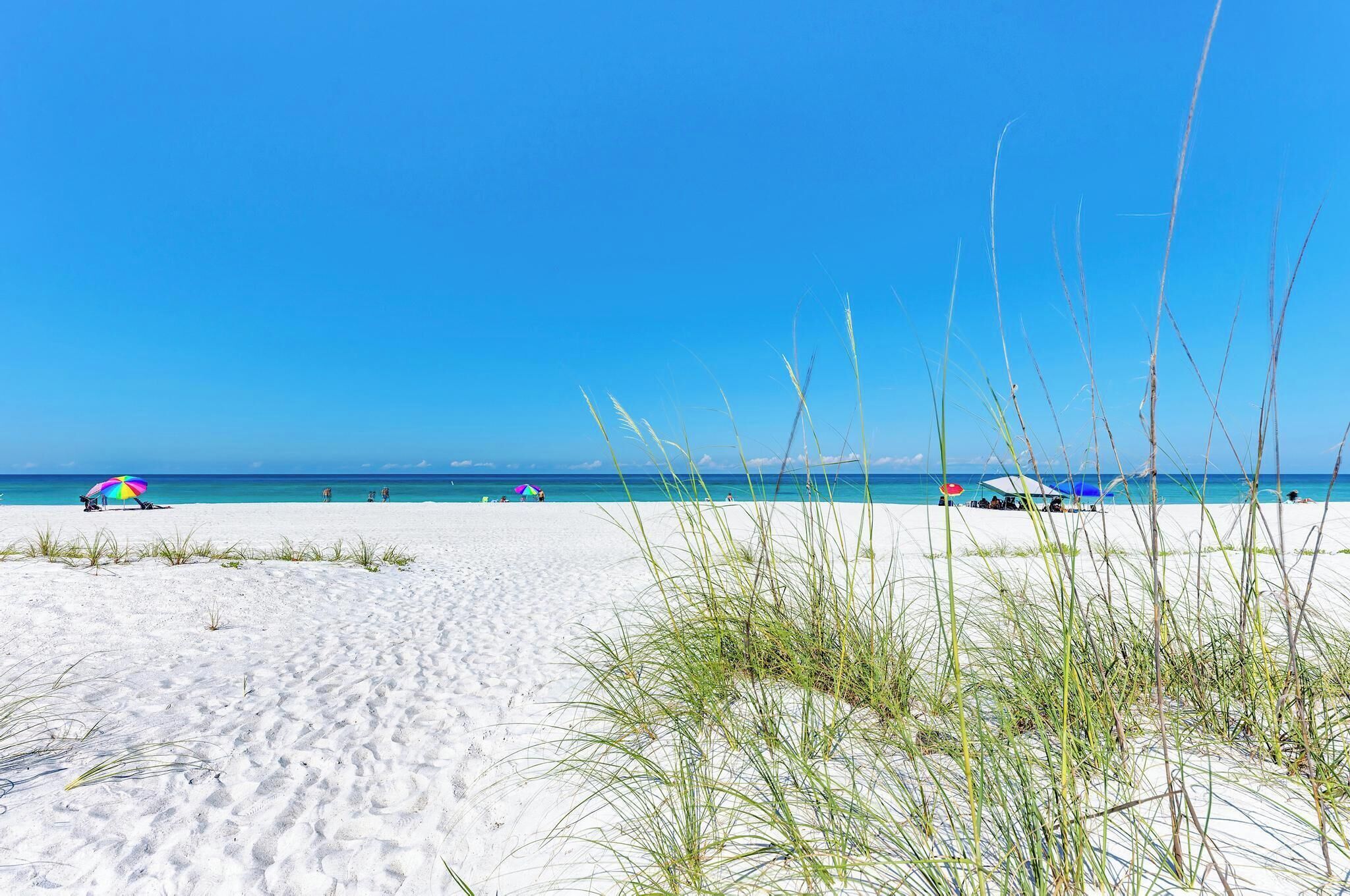 En strand med hvidt sand, klar blå himmel og et par parasoller.