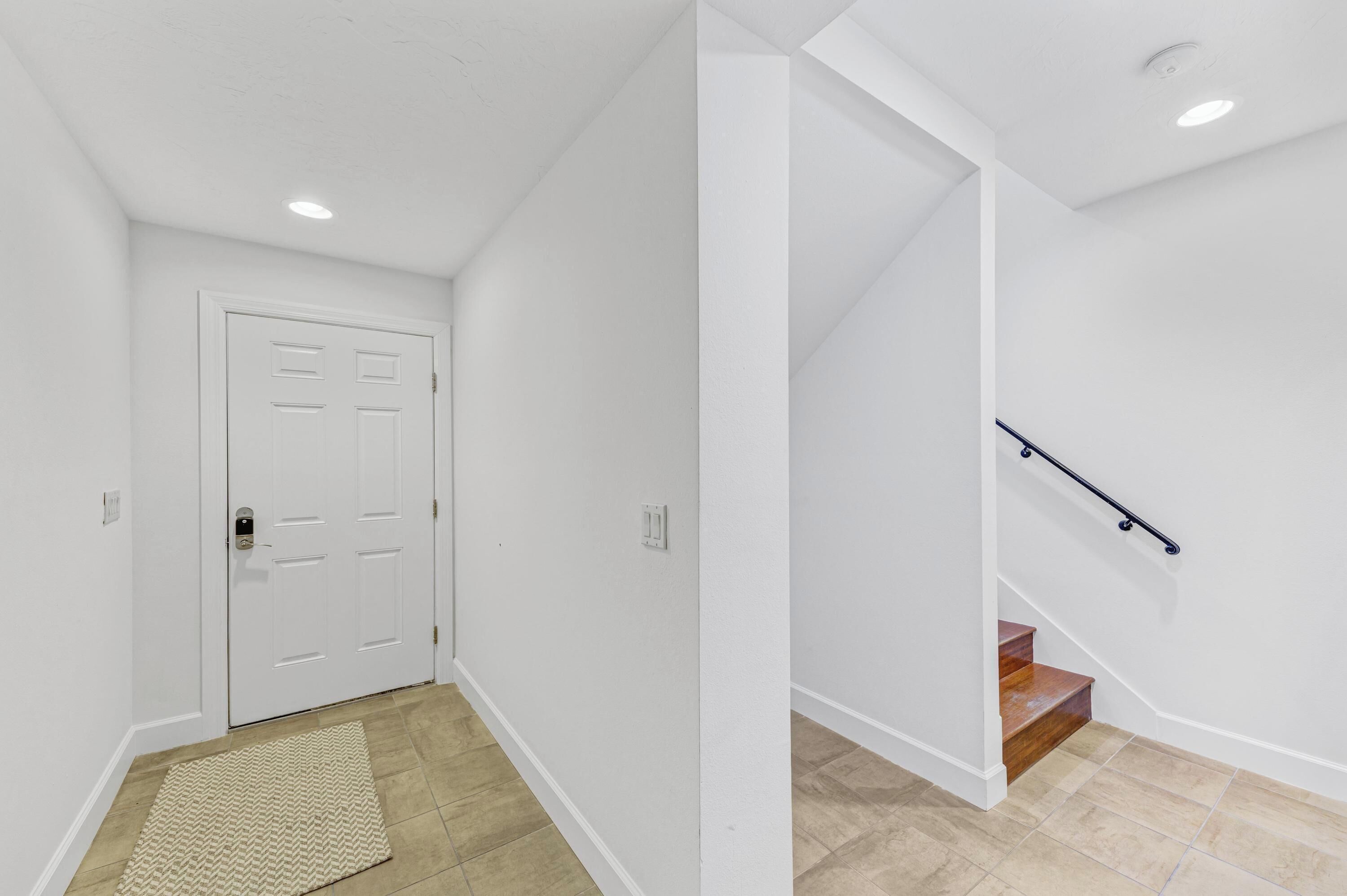 A hallway with a white door and a wooden staircase with a black handrail.