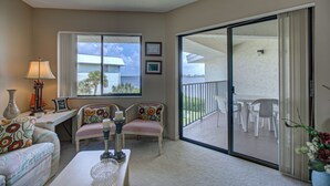 Un amplio salón con sofá, sillas, una mesa de centro y un balcón con mobiliario exterior.