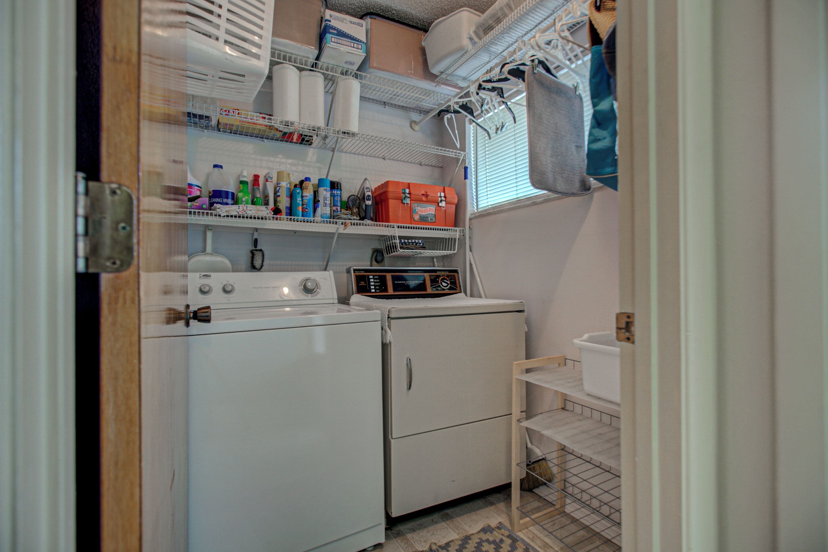 A laundry area with a washing machine, dryer, and shelves with various items.