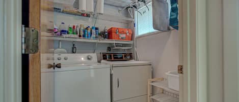 A laundry area with a washing machine, dryer, and shelves with various items.