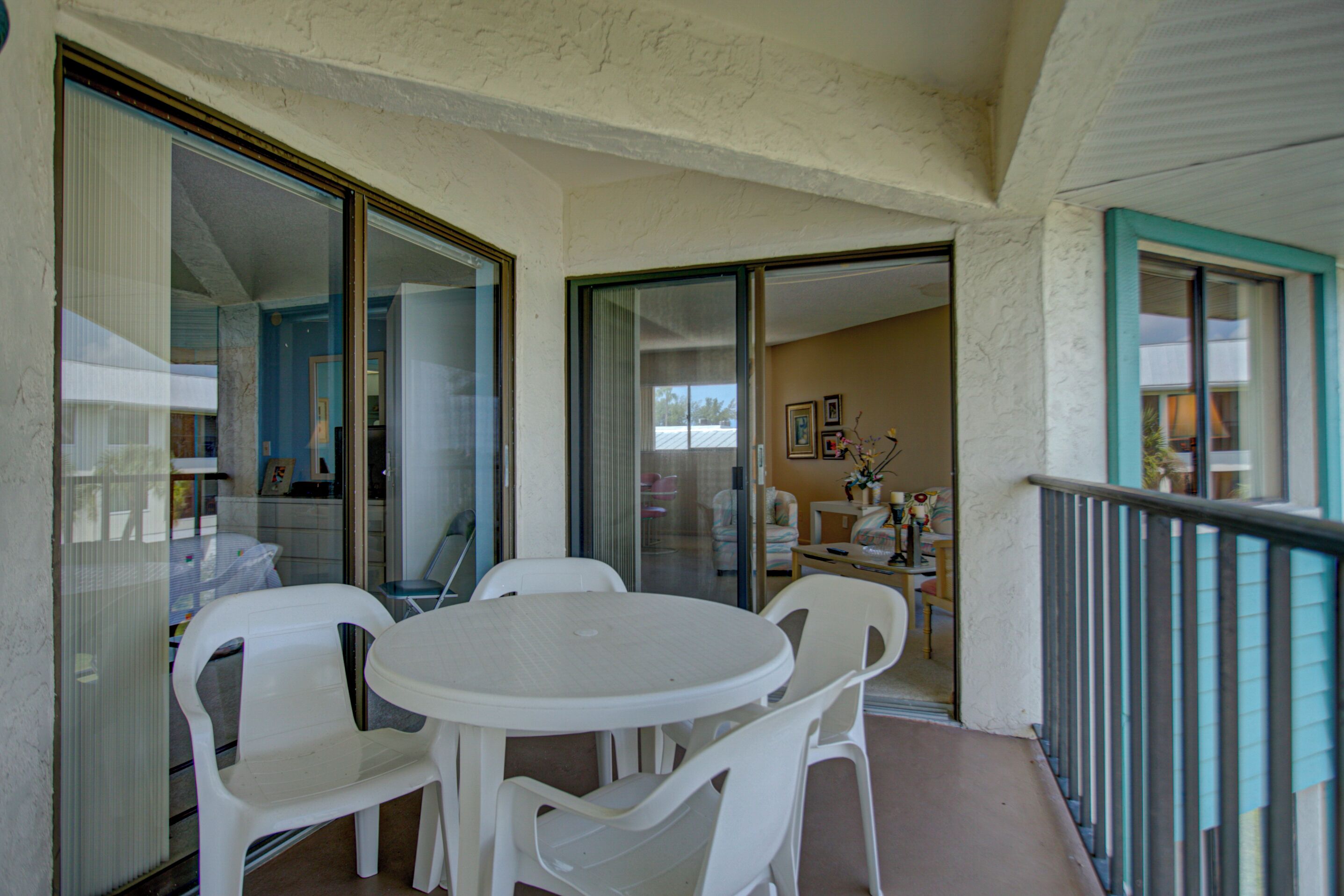 A balcony with a white table and chairs, glass doors leading to an interior room, and a view of the outside.
