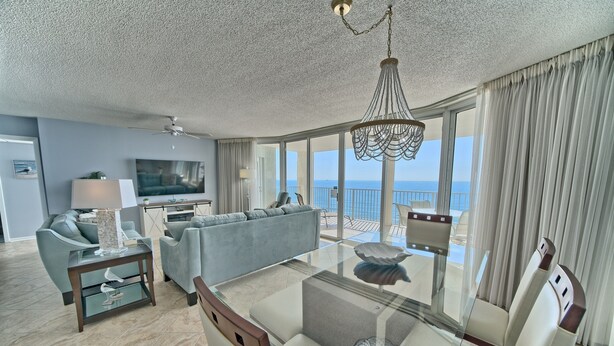 Una sala de estar moderna con un sofá, una mesa de centro de vidrio, un televisor y un balcón con vista al mar.