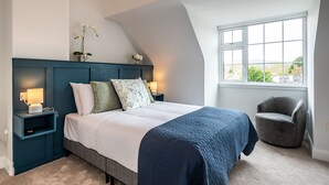 A bedroom with a bed, nightstands, a chair, and a window with a view. - Modern Elegant Townhouse in Historic Kenmare (Kenmare)