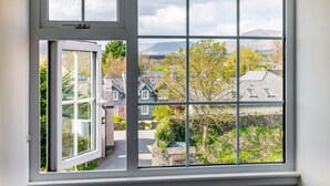 A view through a window with a white frame and multiple panes, overlooking a residential area with houses, trees, and distant mountains. - Modern Elegant Townhouse in Historic Kenmare (Kenmare)