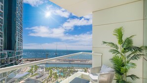 Un balcon offrant une vue sur un paysage urbain moderne, une étendue d’eau et un ciel dégagé.