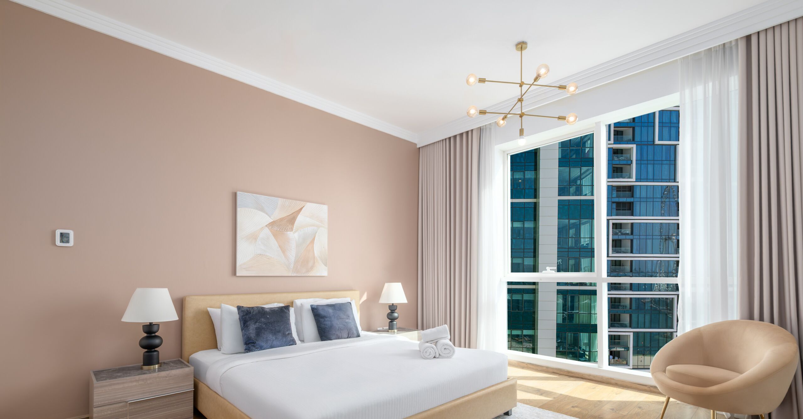 A modern hotel room with a large bed, two bedside tables with lamps, a large window with curtains, and a view of a building.