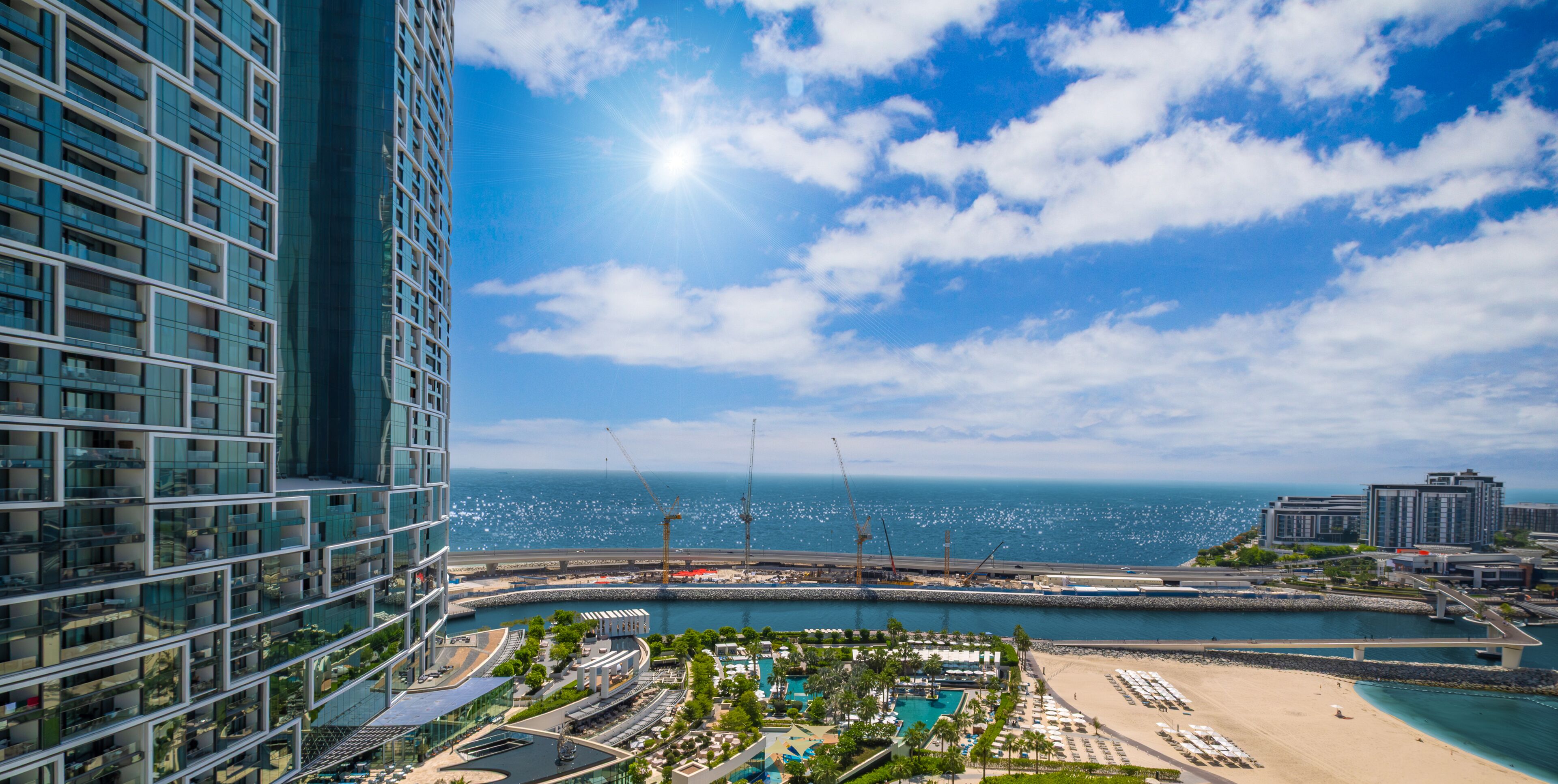 A high-rise building with a view of the sea and a beach area with a pool and lounge chairs.