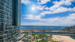 Un immeuble de grande hauteur offrant une vue sur la mer et une plage aménagée avec une piscine et des chaises longues.
