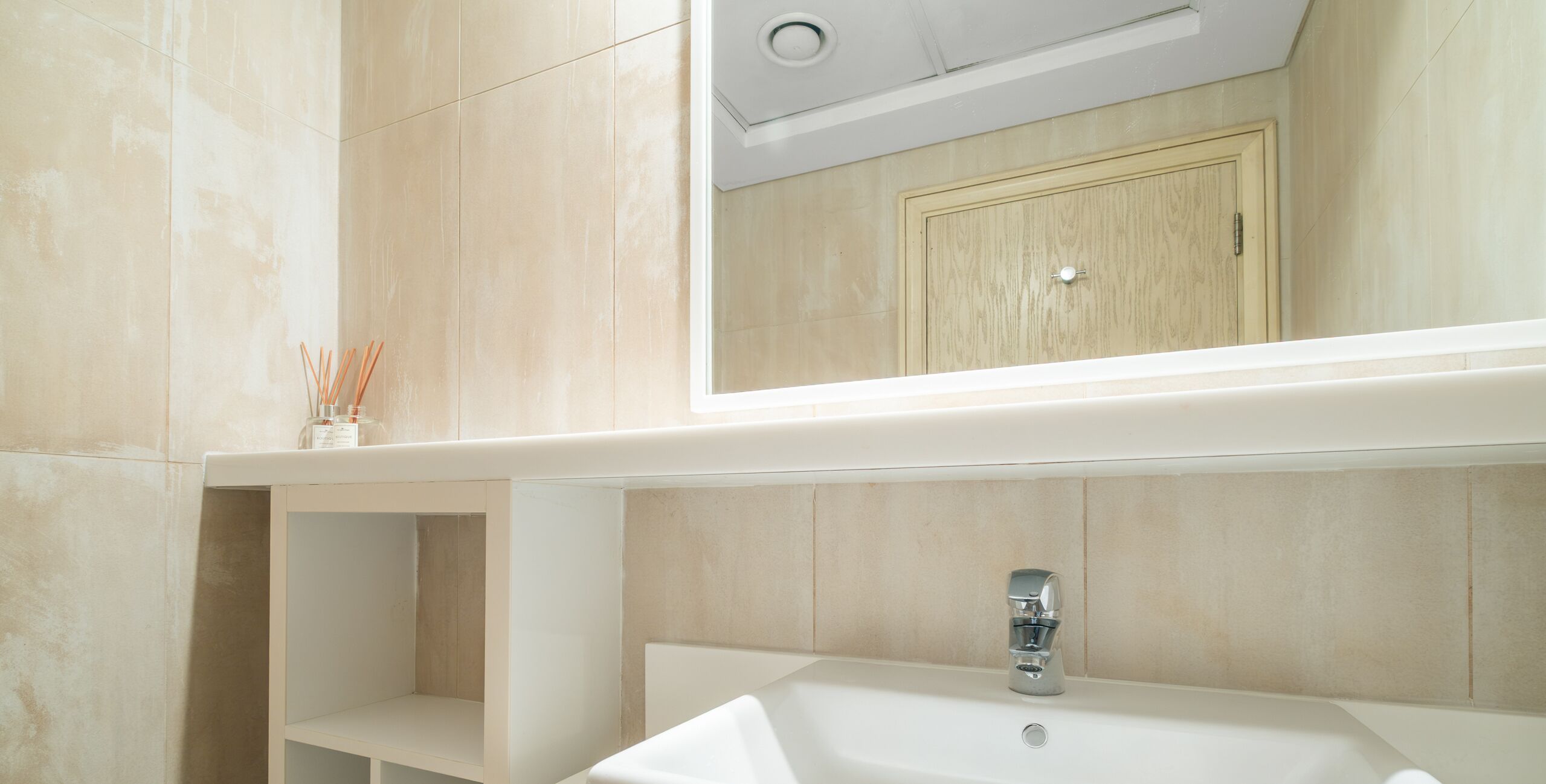 Un bagno moderno con un lavandino bianco, uno specchio sopra e un armadietto in legno.